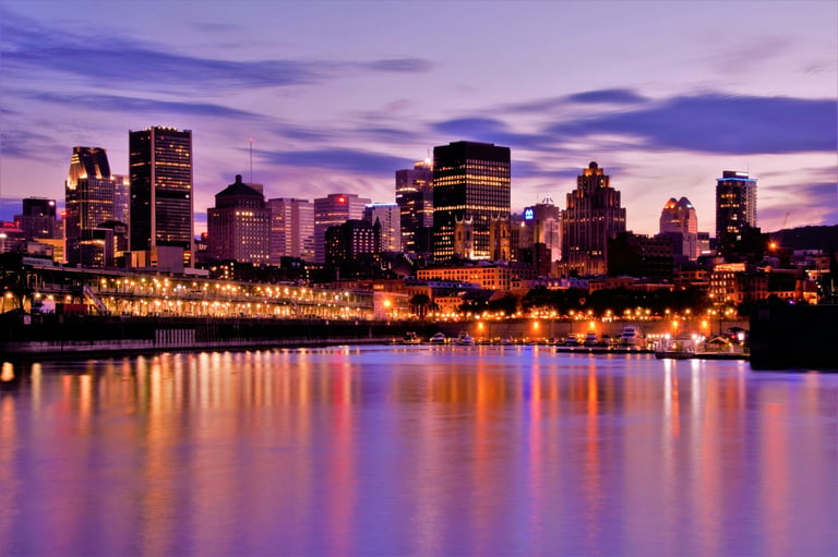 City skyline at dusk with illuminated buildings reflected in calm water under purple twilight sky